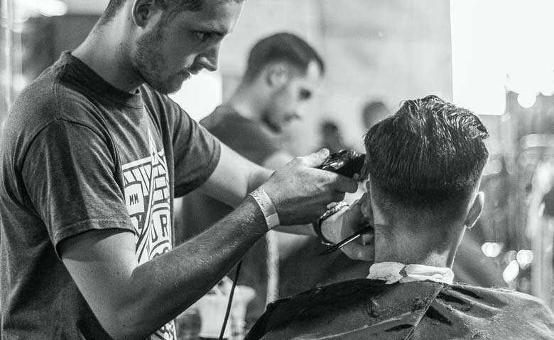 A man getting his hair cut by another man.