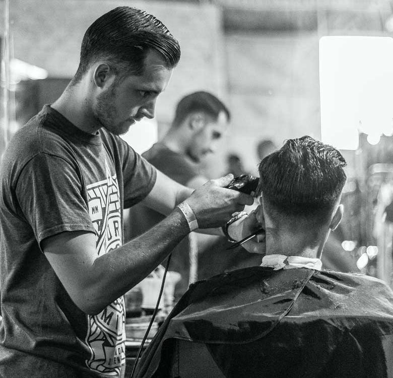 A man getting his hair cut by another man.