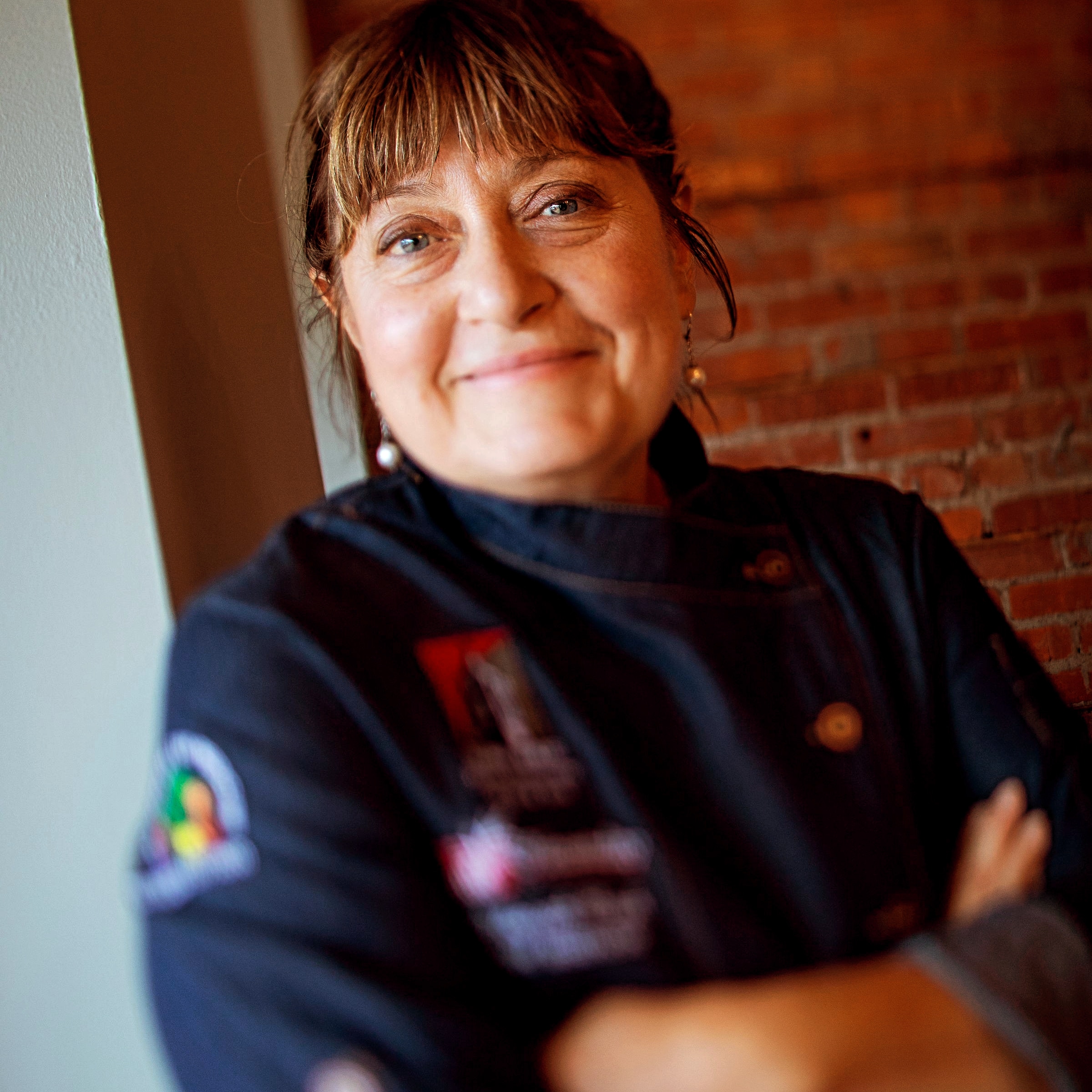 A woman in black jacket standing next to brick wall.